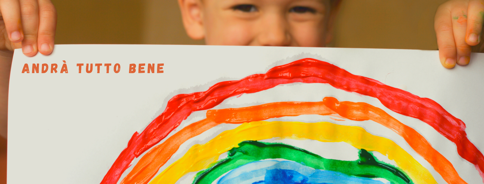 Imamgine di un bambino che tiene nelle mani un disegno di un arcobaleno "Andrà tutto bene"