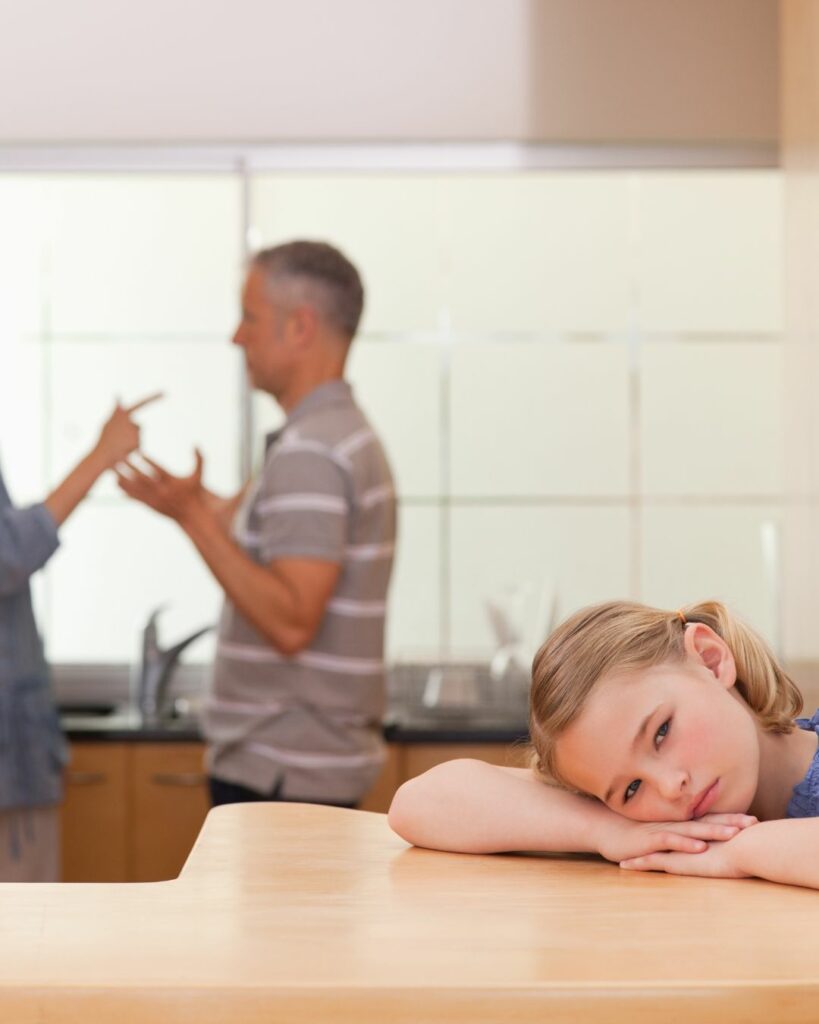 Bambina in primo piano e coppia di genitori che litiga sullo sfondo - Parent Training